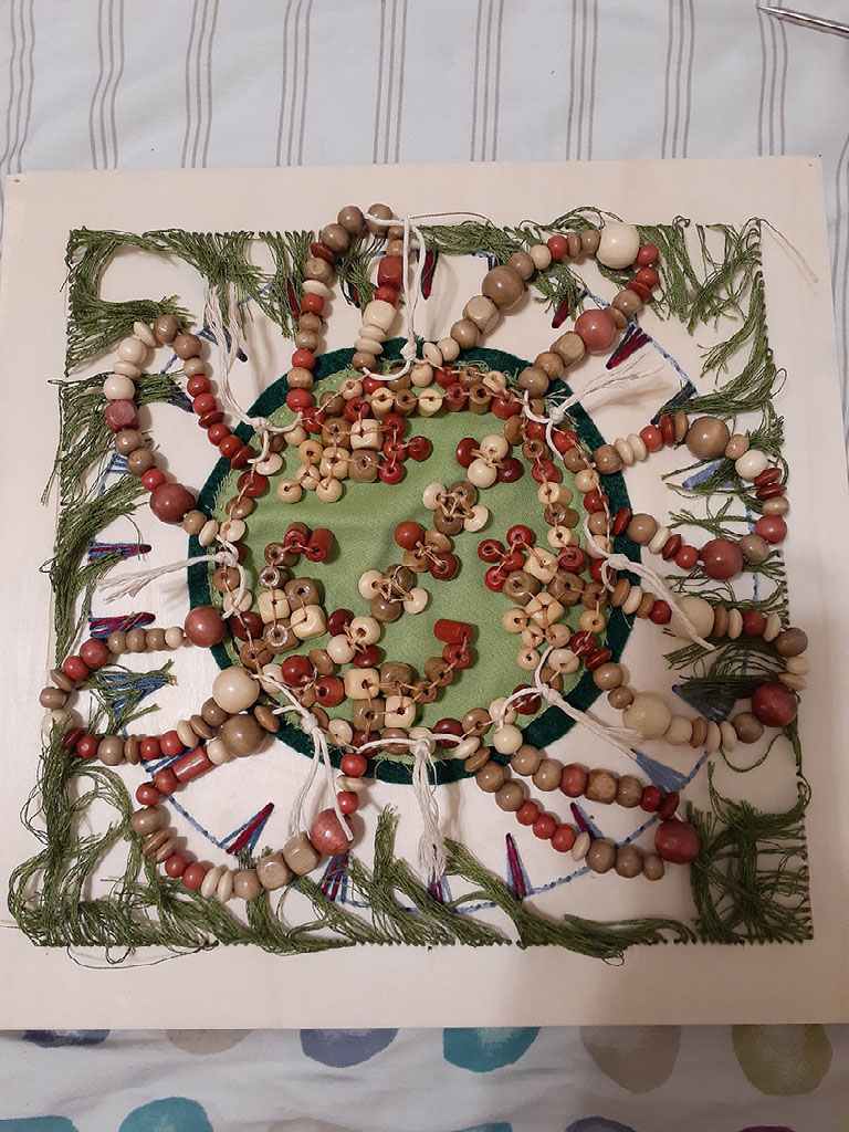 Finished project. Green threads representing treaties, embroidered spikes, and bead work in the center as it extends out to treaties and spikes.