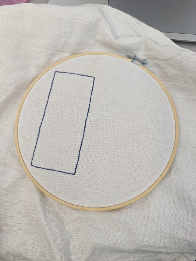 The outline of a blue rectangle created in backstitching on the fabric in the hoop