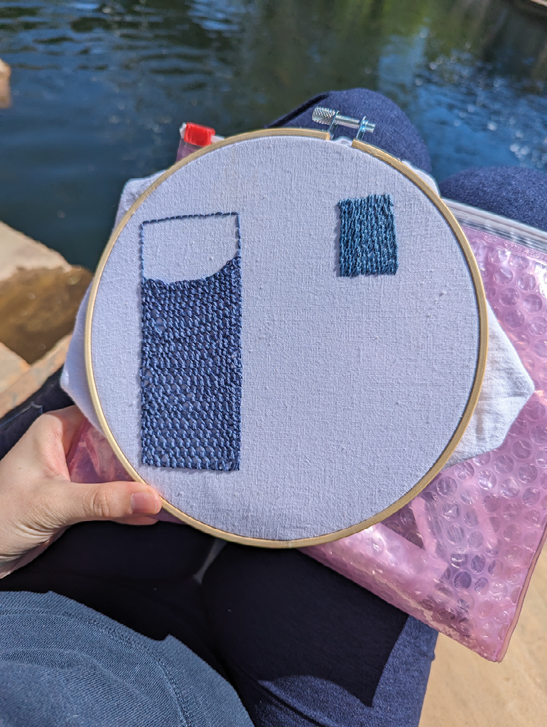 Two embroidered blue rectangles in different shades. On the left, the rectangle is almost completely filled in with detached buttonhole stitching. On the right, is the start of an incomplete rectangle made of stem stitching.