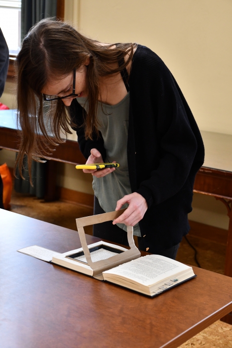A woman using her phone to view an artifact's augmented reality as part of the Bibliocircuitry: Old Books, New Stories showcase